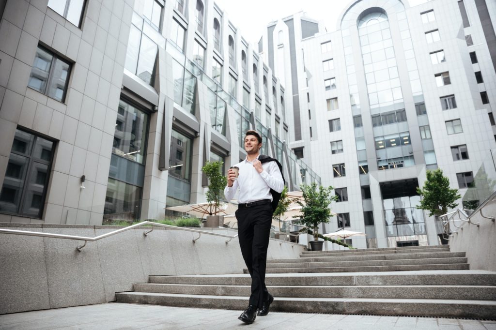 Happy young businessman walking and drinking coffee